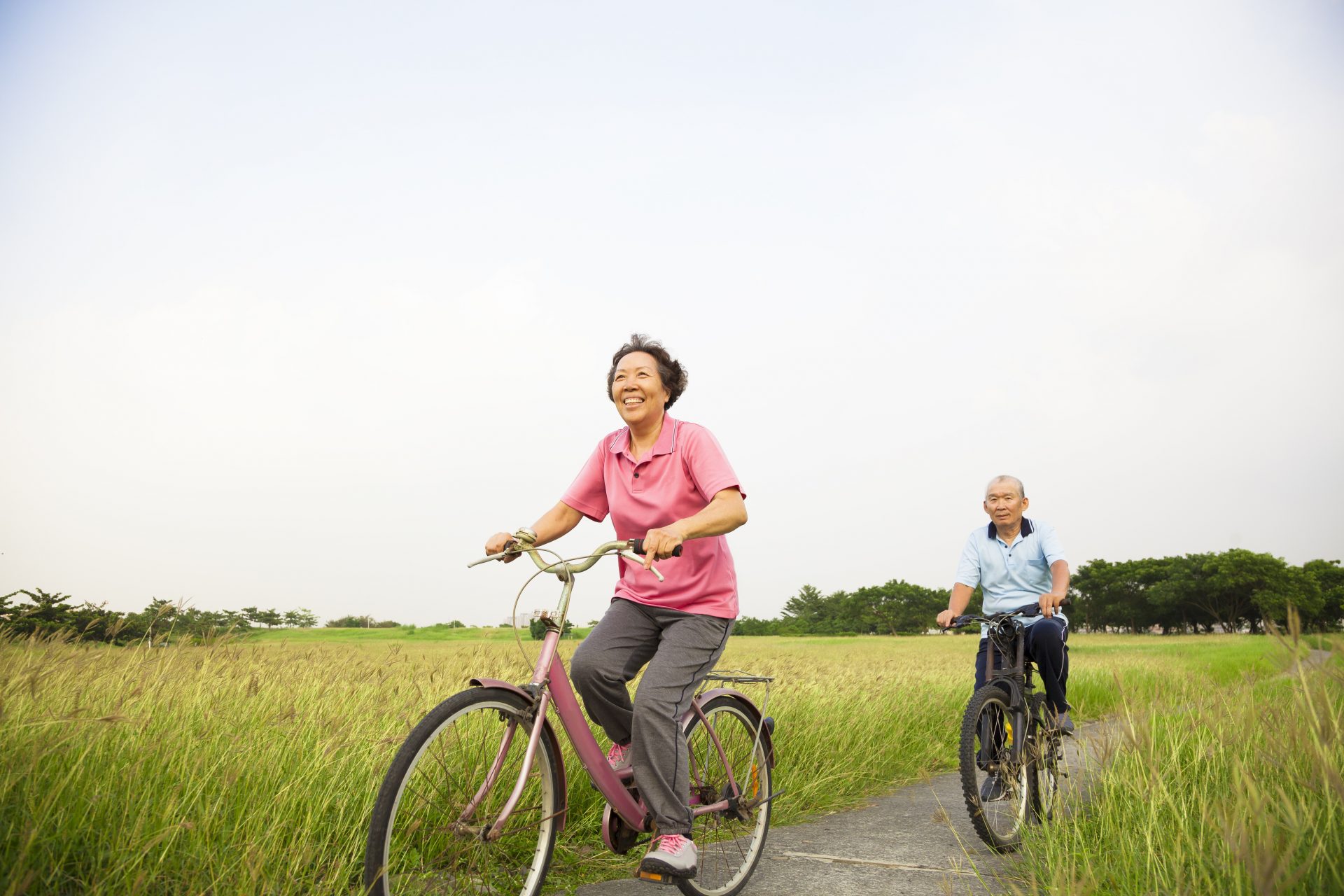 Happy Asian elderly seniors couple biking in the park