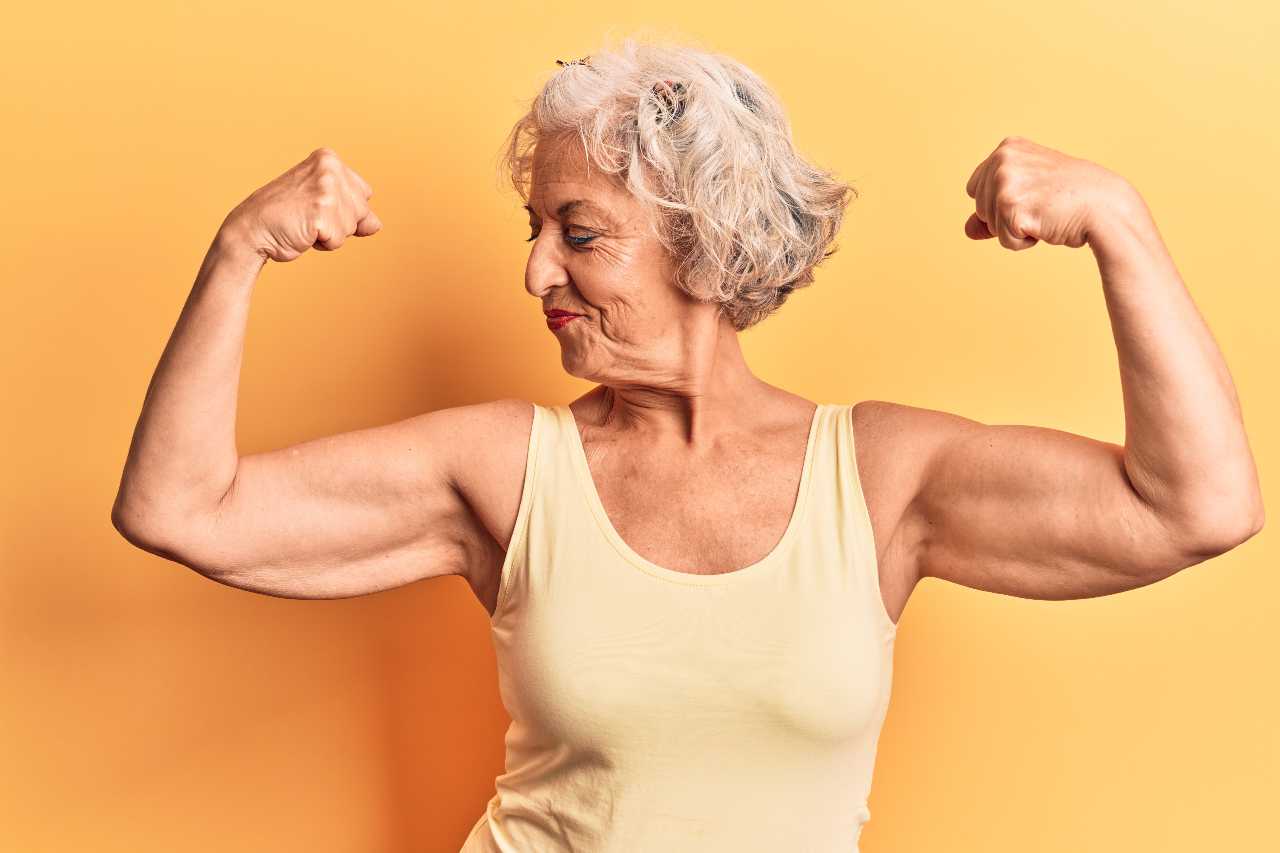 Senior grey-haired woman wearing casual clothes showing arms muscles smiling proud. fitness concept